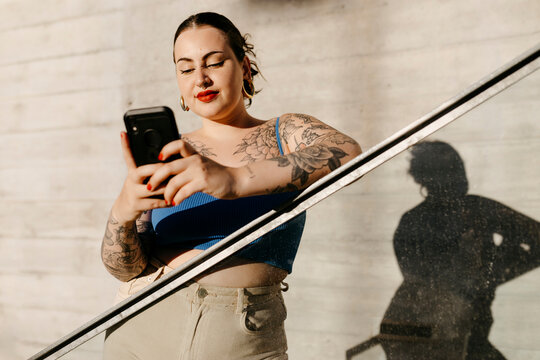 Tattooed plus size woman browsing smartphone on stairs
