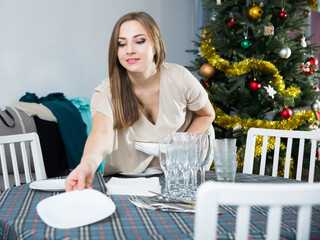 Portrait of attractive young woman preparing table for celebration of Christmas at home