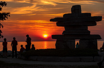 Silhouette of people watching the sunset on the shore of waterfront park with Inukshuk