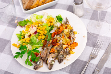Appetizing fried blue whiting with vegetables, served with a light salad of canned corn, Peking cabbage and lettuce leaves