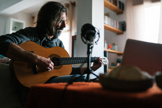 Bearded man recording guitar song at home