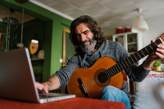 Cheerful bearded guitarist using laptop