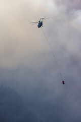 Wildfire Service Helicopter flying over BC Forest Fire and Smoke on the mountain near Hope during a hot sunny summer day. British Columbia, Canada. Natural Disaster