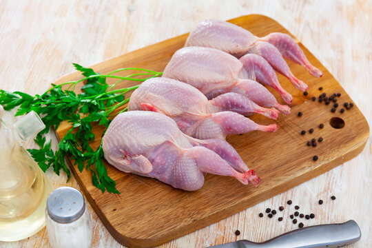 Uncooked quails on wooden board with parsley and black pepper. Home kitchen, preparing food.