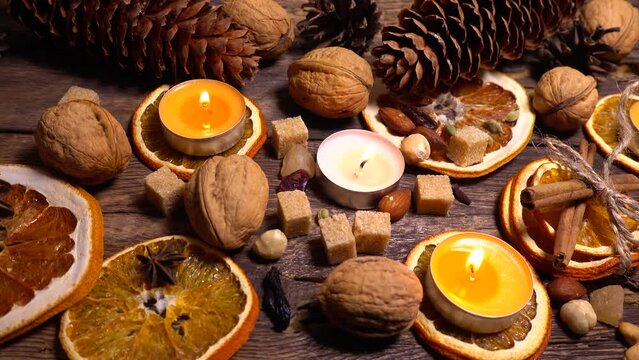 Natural composition in hygge style with candles, orange slices, fragrant spices, walnuts and pine cones on an old vintage wooden board background.