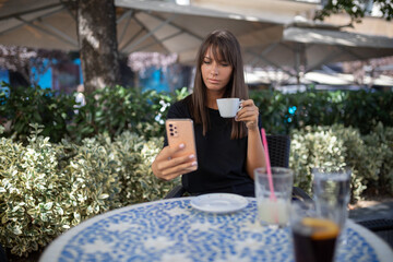 Morning in cafe - attractive woman in black drinkin coffe and make selfie photo for social networks