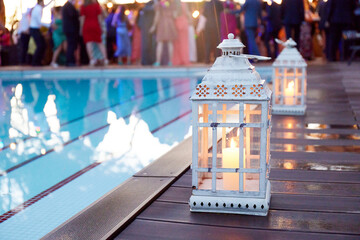 Candlelit lanterns by a pool during a wedding reception