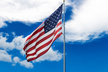 Large American flag waving in the wind against a cloudy blue sky.