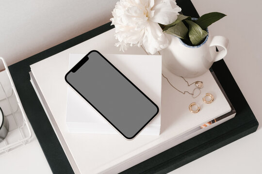 Cellphone with jewelry and flower vase on white desk