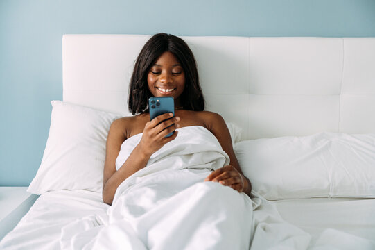 black woman using smartphone in bed