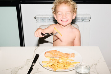 Cheerful toddler holding french fries on fork.