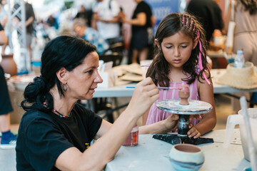 Woman painting on pottery near girl
