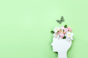 Cardboard silhouette of human head decorated with flowers and butterfly on green background. World...
