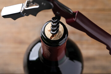 Opening wine bottle with corkscrew on blurred background, closeup