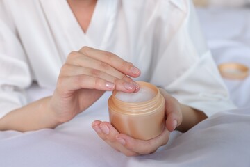 Woman taking hand cream from jar indoors, closeup