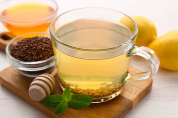 Cup of aromatic buckwheat tea, mint and granules white wooden on table, closeup