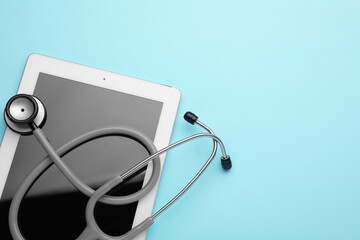 Computer tablet and stethoscope on turquoise background, top view. Space for text