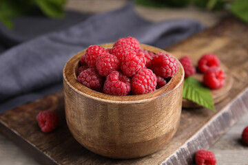 Bowl of fresh ripe raspberries on wooden board, closeup