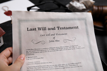 Woman holding last will and testament at black table, closeup - obrazy, fototapety, plakaty