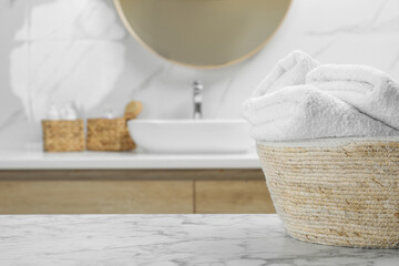 Wicker basket with folded bath towels on white marble table in bathroom, space for text