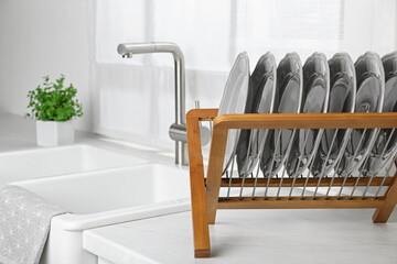 Fototapeta na wymiar Wooden holder with grey plates on countertop near sink in kitchen