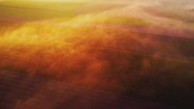 Thick fog covering colorful farm fields with orange glaze from rising sun. Morning landscape of Roztocze Poland. Birdseye view. Horizontal shot. High quality 4k footage