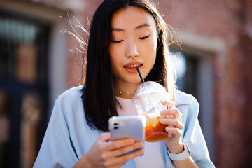 Girl with drink chatting online in cellphone  