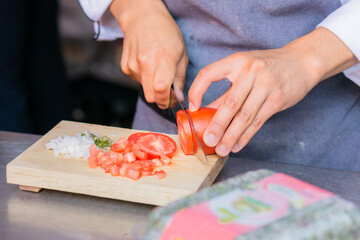 Obraz na płótnie Canvas Hands of an unrecognizable person cutting tomato, chili and onion on a board.