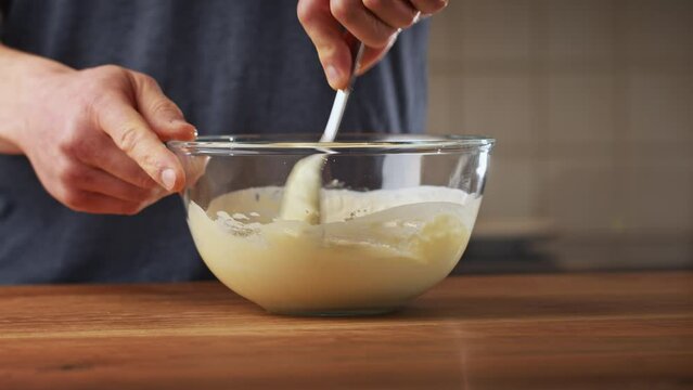 A male home chef making Bulgarian moussaka in his kitchen. Closeup shot - preparing topping with yogurt, eggs and flour.