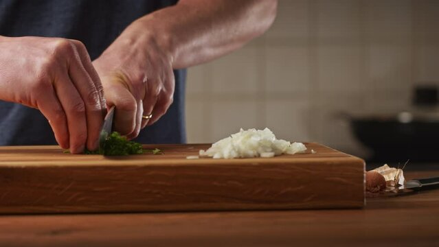 A male home chef making Bulgarian moussaka in his kitchen. Closeup shot - chopping fresh parsley on a wooden cutting board.