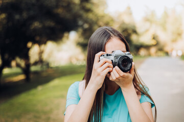 Young tourist girl, taking photos with a vintage film camera while walking in the park.