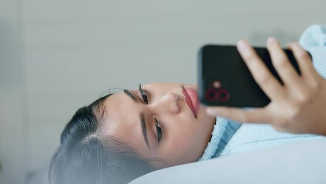 Stress, headache and anxiety by woman texting on phone, reading message and lying on a bed in her home. Anxiety, bad news and sad girl suffering with mental health problem and migraine while browsing