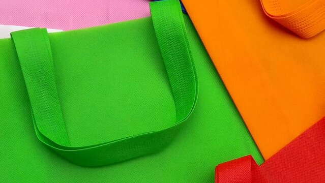 pink, green, orange, white,red and blue polypropylene bags. pile of tote bags of non-woven fabric with folded straps