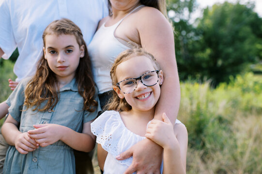 Little happy girl with glasses smiling while holding her mother's arm