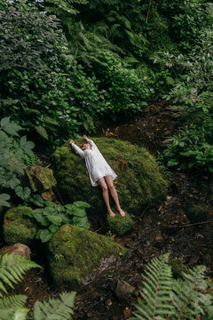 A dreamy girl in old-fashioned white lies in a picturesque forest