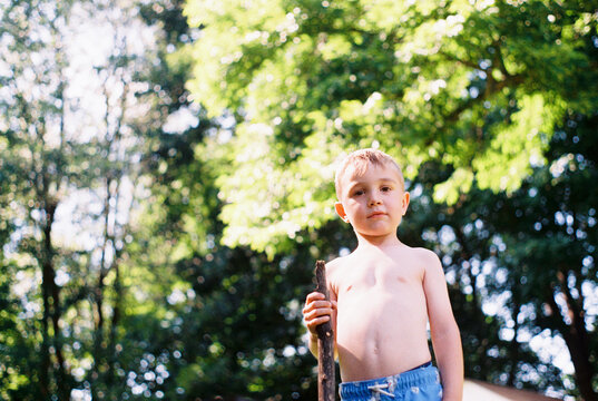 Little boy holding a stick while shirtless and in swimming trunks