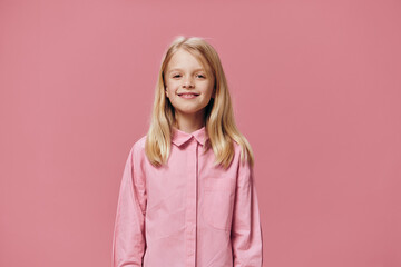 a beautiful, small, funny girl stands in a pink shirt on a pink background and smiles sweetly