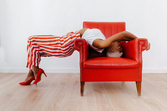Calm stylish black woman lying on armchair in studio