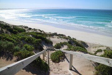 Beach stairs going to white beach through native vegetation, with a turquoise calm see in South...