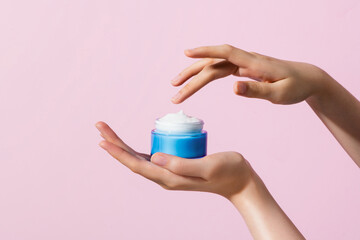 Woman hand holding jar moisturizer cream isolated on pink background.