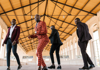 Fashionable black men in stylish suits dancing in hall