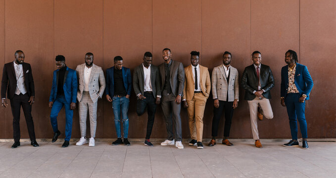 Confident black men in stylish outfits near wall