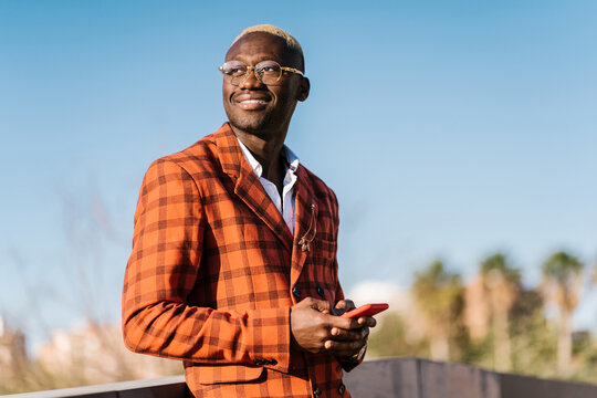 Smiling black man in suit browsing smartphone on street