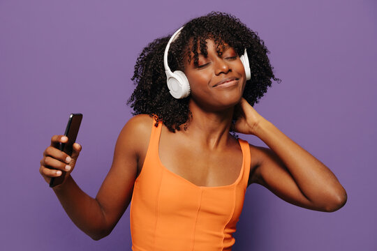 Cheerful black woman in headphones with smartphone