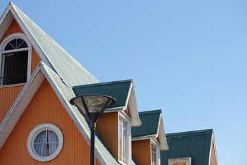 Casa antigua en Valpara&iacute;so de color anaranjado y techo verde con varias ventanas, un farol delante y el cielo azulado