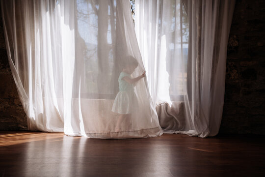 Little girl playing hidden behind curtains