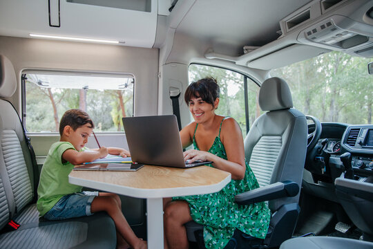 Mother and son sitting in van and working on laptop during road trip