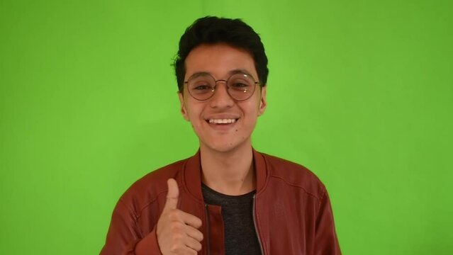 Joven hombre sonriente con gafas asintiendo con las manos en un fondo verde