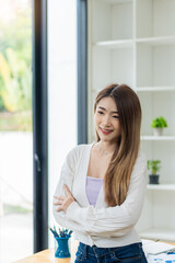 Smiling Asian woman standing with her arms crossed looking at the camera at work
confidently