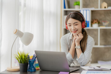 An Asian accountant or office worker wears headphones online with a laptop and listens to music during breaks.